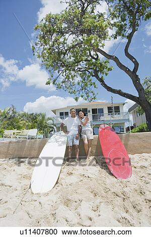 Stock Image - A couple together standing with surfboards. Fotosearch