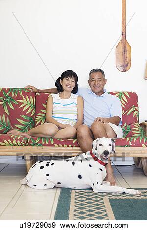 Stock Photo - A couple sitting on sofa with dog. Fotosearch