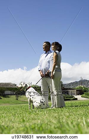 Stock Image - A couple standing in lawn with dog. Fotosearch