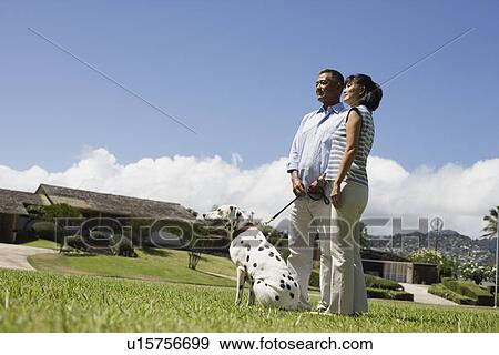 Stock Photo - A couple standing in lawn with dog. Fotosearch