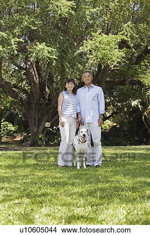 Picture - A couple standing in park with dog. Fotosearch