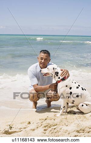 Stock Image - Man crouching with dog at beach. Fotosearch
