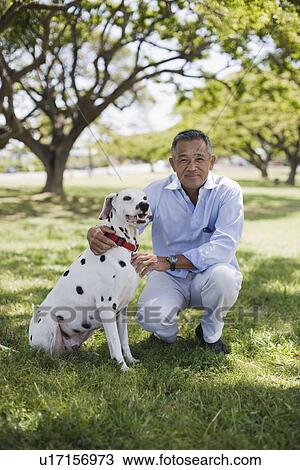 Stock Image - Man sitting with dog in park. Fotosearch