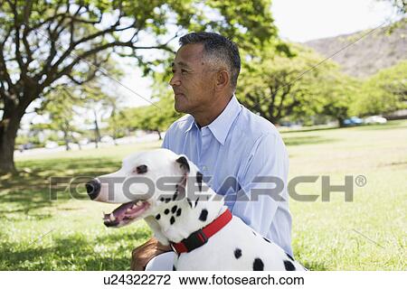 Stock Image - Profile of man sitting with dog in park. Fotosearch