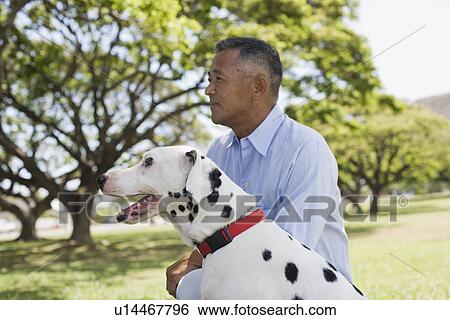 Stock Photograph - Profile of man sitting with dog in park. Fotosearch