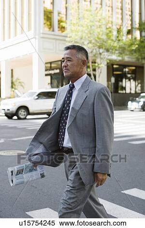 Stock Photography - Businessman walking on road holding newspaper. Fotosearch