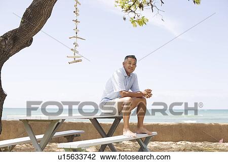 Stock Image - Mature man sitting on table. Fotosearch