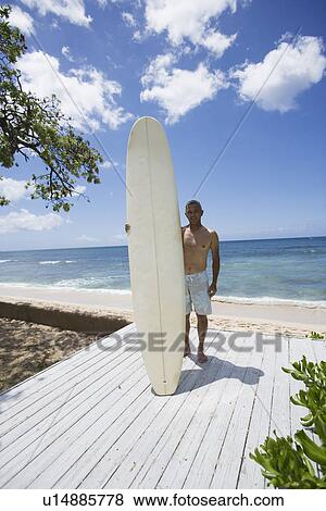 Stock Photo - Mature man standing with surfboard. Fotosearch