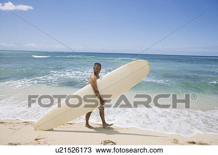 Stock Image - Mature man walking with surfboard at beach. Fotosearch