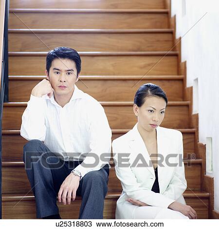 Stock Image - Businesswoman and a businessman sitting on a staircase. Fotosearch