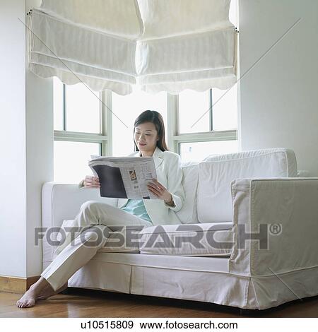 Businesswoman sitting on a couch reading a newspaper View Large Photo Image Stock Photo - Businesswoman sitting on a couch reading a newspaper. Fotosearch