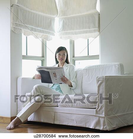 Businesswoman sitting on a couch with a newspaper in her hand View Large Photo Image Picture - Businesswoman sitting on a couch with a newspaper in her hand. Fotosearch