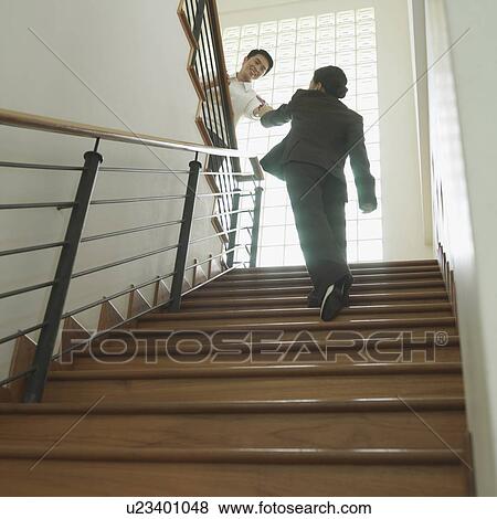 Low angle view of a businessman shaking hands with a businesswoman on a staircase View Large Photo Image Stock Photo - Low angle view of a businessman shaking hands with a businesswoman on a staircase. Fotosearch