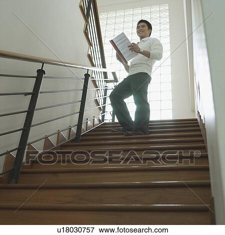 Stock Photo - Low angle view of a businessman standing on a staircase with a file in his hand. Fotosearch