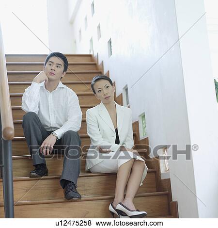 Stock Photo - Low angle view of a businesswoman and a businessman sitting on a staircase. Fotosearch