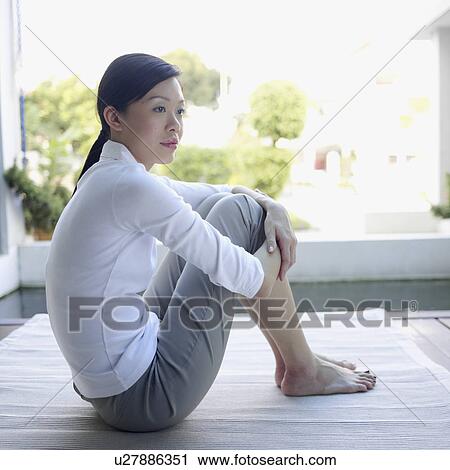 Stock Image - Side profile of a young woman sitting on the floor. Fotosearch