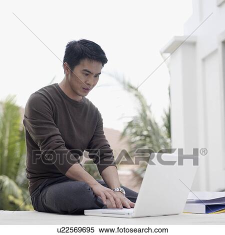 Young man sitting on the floor working on a laptop View Large Photo Image Stock Photography - Young man sitting on the floor working on a laptop. Fotosearch