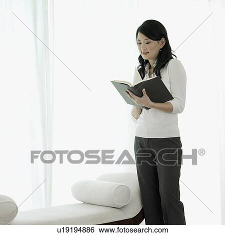 Stock Photograph - Young woman standing and reading a book. Fotosearch