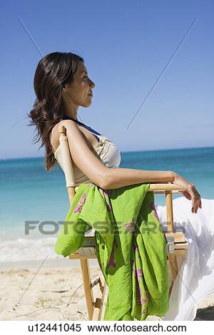 Stock Photography - A young woman sitting on chair at beach. Fotosearch