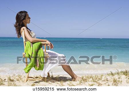 Stock Photography - A young woman sitting on chair at beach. Fotosearch
