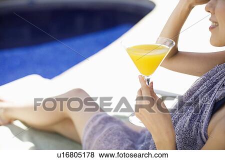 Stock Photo - A young woman sitting with drinks beside swimming pool. Fotosearch