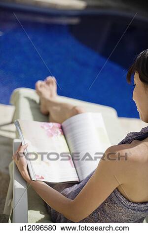Stock Image - Elevated view of a young woman reading a book. Fotosearch