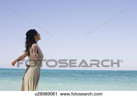 Side view of a young woman standing on beach View Large Photo Image Stock Image - Side view of a young woman standing on beach. Fotosearch