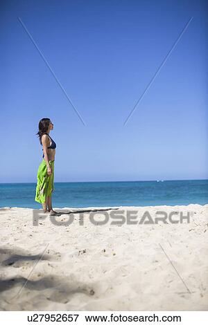 Stock Photo - Side view of a young woman standing on beach. Fotosearch