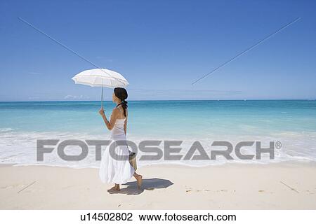 Stock Image - Side view of a young woman walking on beach. Fotosearch