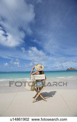 Stock Image - A woman sitting on chair on beach. Fotosearch