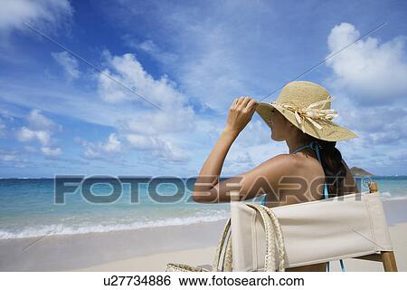 Stock Photograph - A woman sitting on chair on beach. Fotosearch