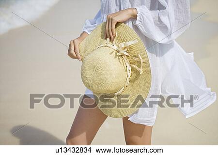 Picture - A woman standing on beach with hat in hand. Fotosearch