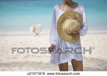 A woman standing on beach with hat in hand View Large Photo Image Stock Photo - A woman standing on beach with hat in hand. Fotosearch
