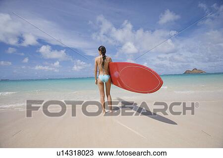 A woman standing on beach with surfboard in hand View Large Photo Image Stock Image - A woman standing on beach with surfboard in hand. Fotosearch
