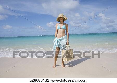 Stock Image - A woman standing on beach with surfboard. Fotosearch