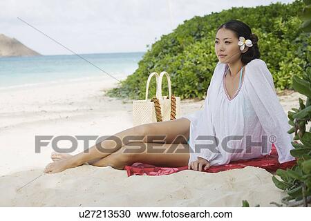 Stock Image - A young woman sitting at beach looking away. Fotosearch
