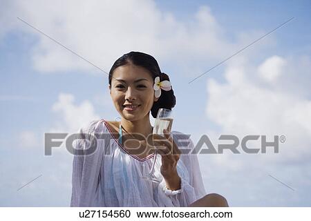 Stock Image - Low angle view of a young woman holding wineglass. Fotosearch
