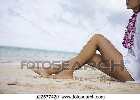 Stock Photo - Low section of a woman sitting at beach. Fotosearch