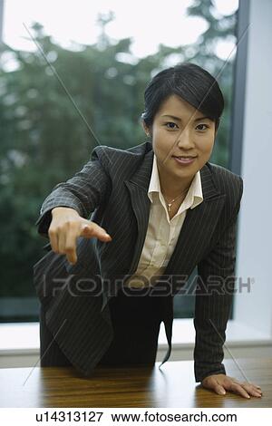 Stock Photo - A professional woman pointing towards something as she smiles at the camera. Fotosearch