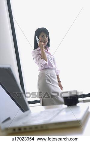 Picture - A woman converses on the mobile phone as she looks at the camera. Fotosearch