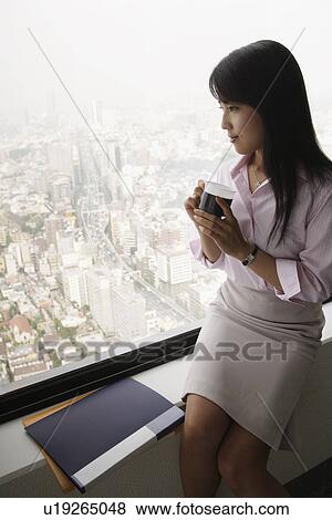 A woman drinking coffee as she is seated near the window View Large Photo Image Stock Photo - A woman drinking coffee as she is seated near the window. Fotosearch