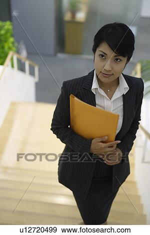 Stock Photo - A woman holding a file stands on the staircase. Fotosearch