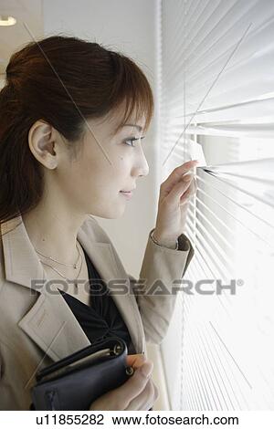 Stock Image - A woman looking outside through the blinds. Fotosearch