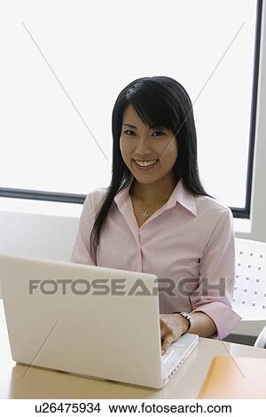 Picture - A woman working over her laptop smiles at the camera. Fotosearch