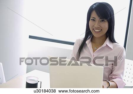 Stock Photo - A woman working over her laptop smiles at the camera. Fotosearch