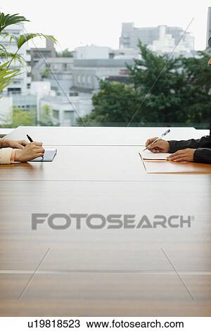 Stock Image - Two people working together on a large wooden table placed in the terrace. Fotosearch