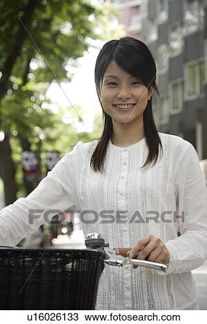 Stock Image - Portrait of a young woman holding bicycle. Fotosearch