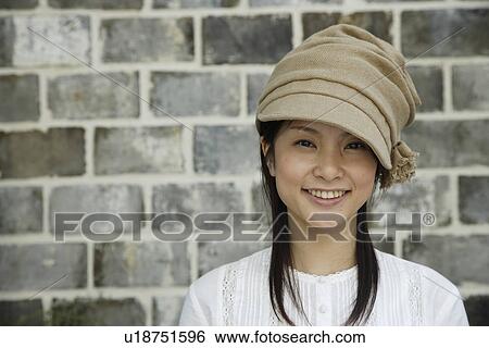Stock Photograph - Portrait of a young woman smiling by brick wall. Fotosearch