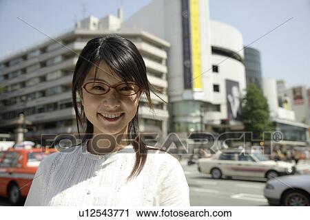Stock Image - Portrait of a young woman smiling with buildings in background. Fotosearch