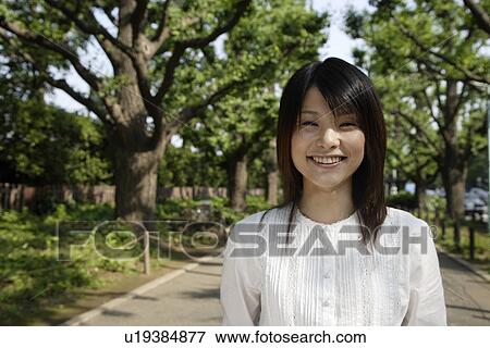Stock Photo - Portrait of a young woman smiling with trees in background. Fotosearch